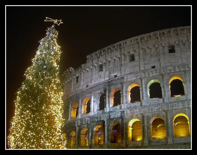 The Roman Colosseum illuminated at night with a beautifully lit Christmas tree in the foreground.