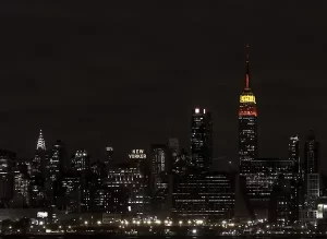 The New York City skyline at night, with the Empire State Building illuminated in red and green holiday colors.