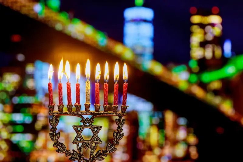 A glowing hanukkiah with multiple candles, celebrating Hanukkah outside a lit New York City.