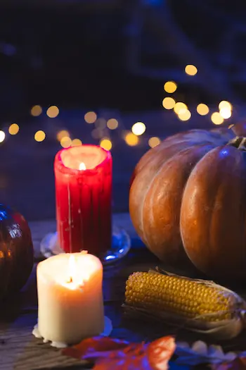 A glowing jack-o’-lantern on a rustic wooden table, decorated with dried corn and fall leaves.