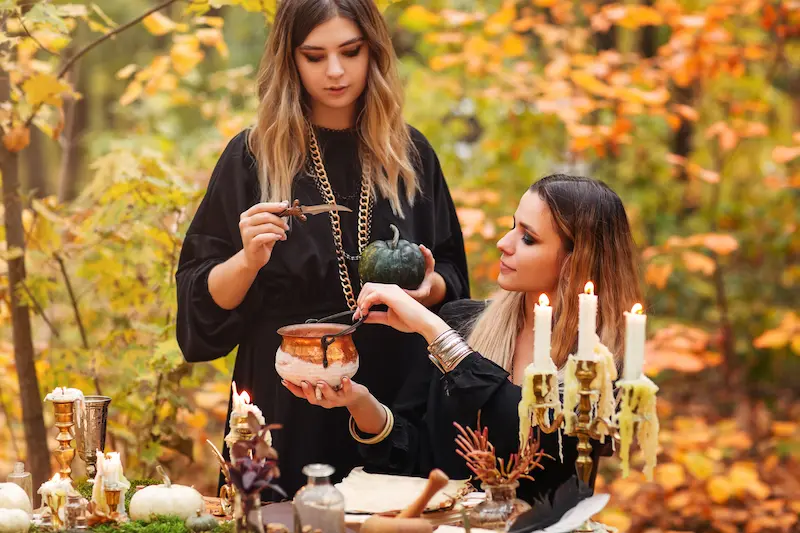 Two girls practicing a Samhain ritual outdoors, surrounded by candles and autumn leaves.